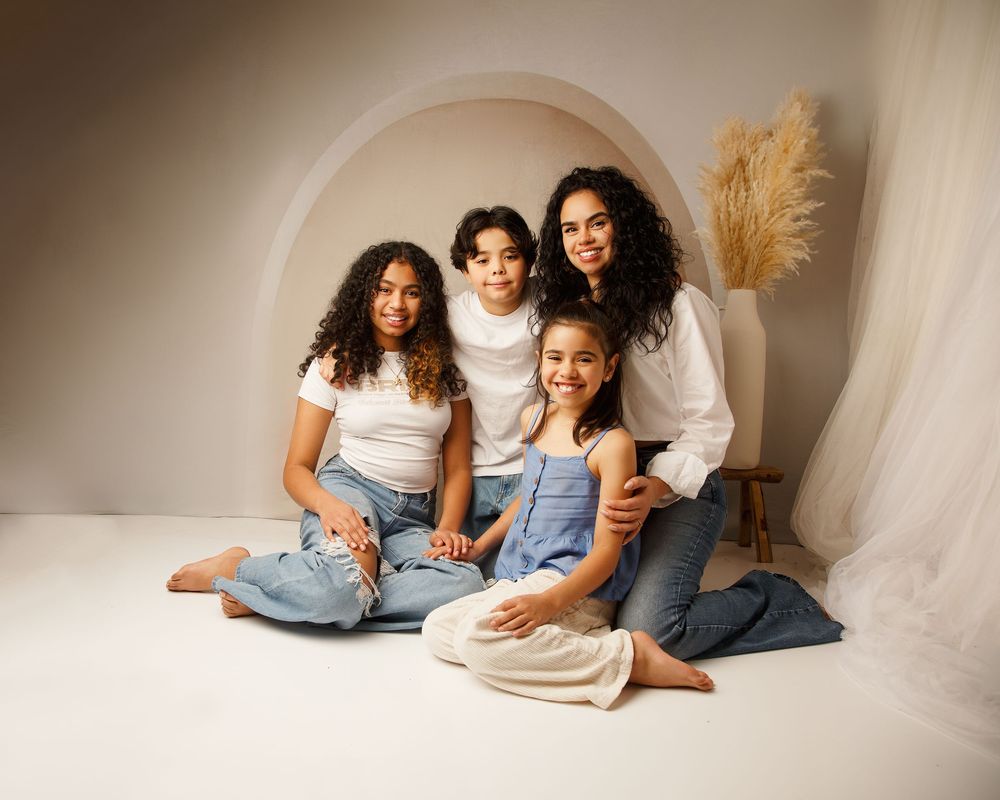 Group sits together on white floor against arched backdrop with pampas grass decoration in modern lifestyle photoshoot.