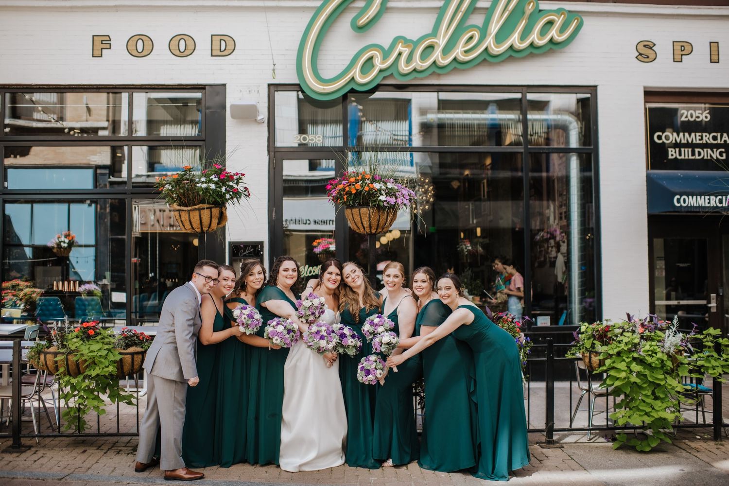 Wedding party poses together outside Cordelia restaurant with emerald green bridesmaids dresses and hanging planters.