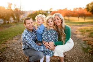 A family poses together on a dirt path during golden hour with autumn trees in the background.