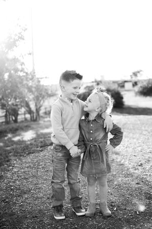 Three young children in casual clothing play together outdoors in black and white vintage style photography.