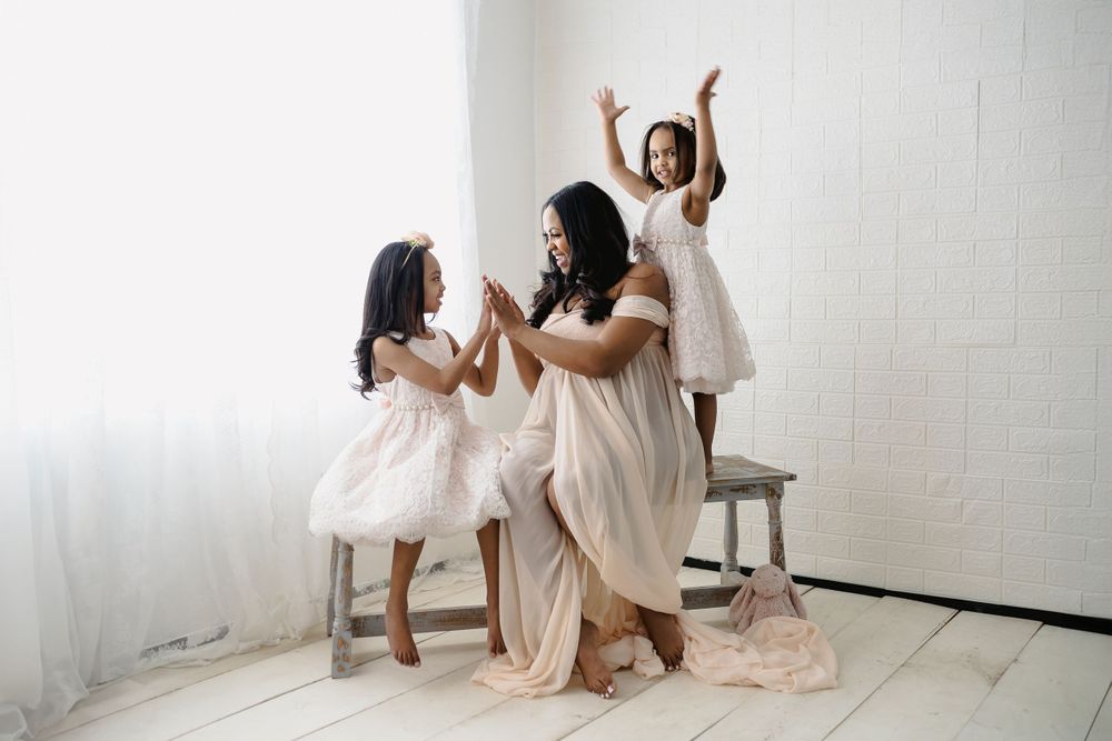 Joyful family photoshoot with children in white dresses posing on stools.