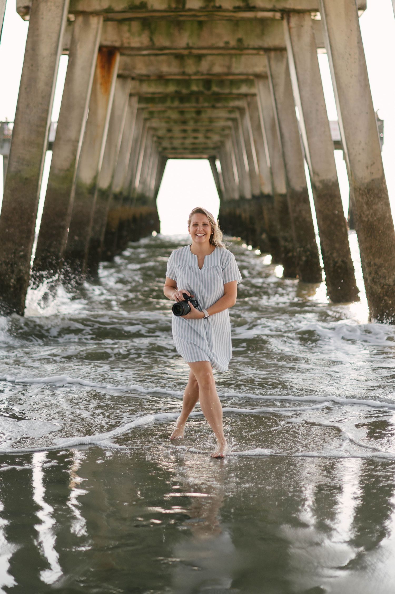 Photographer in striped dress capturing sunset on beach.