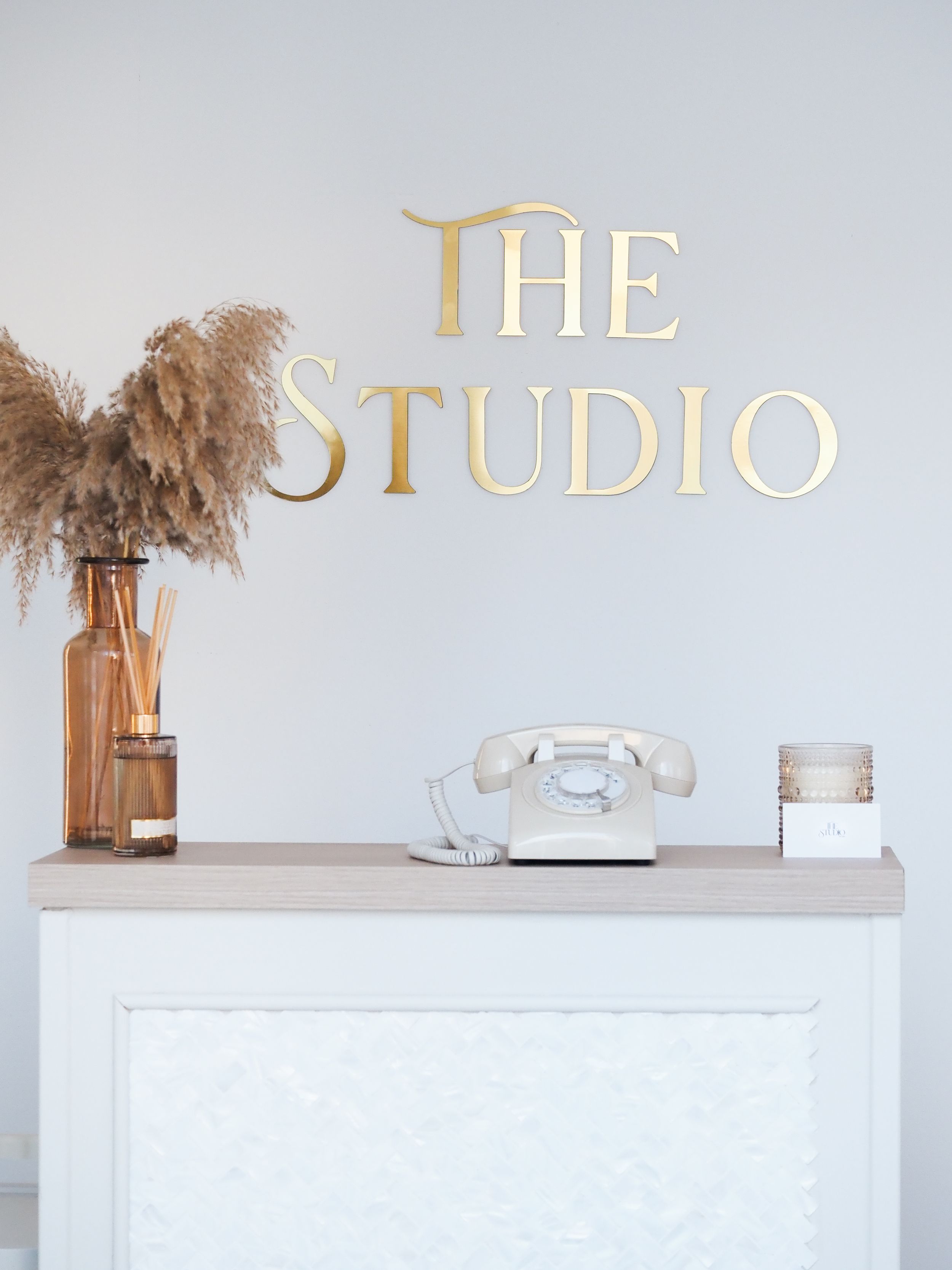 Modern minimalist white retail space with gold lettering spelling 'THE STUDIO' on wall and neutral decor elements.