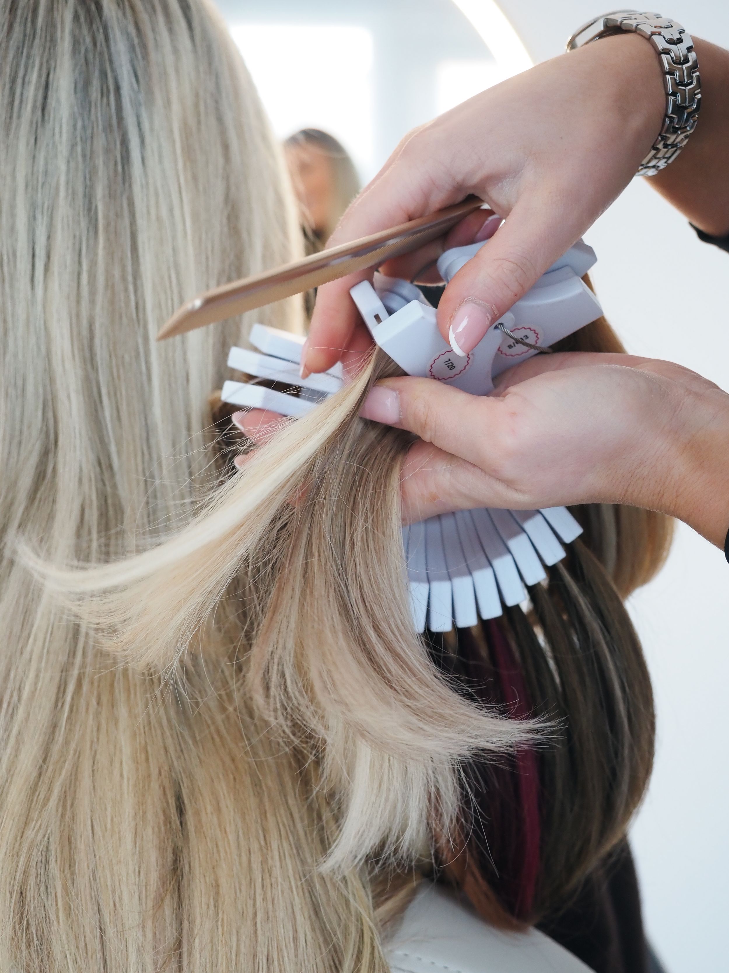 A stylist demonstrates sectioning and applying hair color using foils on blonde and dark two-toned hair.