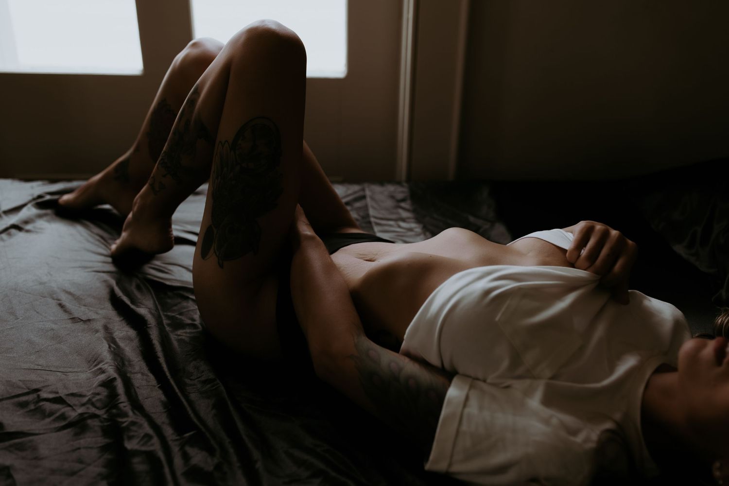 woman laying in bed, legs elongated, toes pointed while pulling up on her shirt