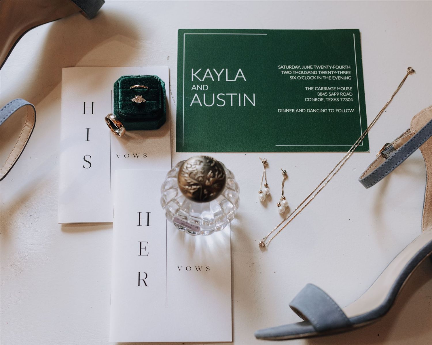 Wedding details flat lay with green invitation, rings, and blue shoes on white surface.