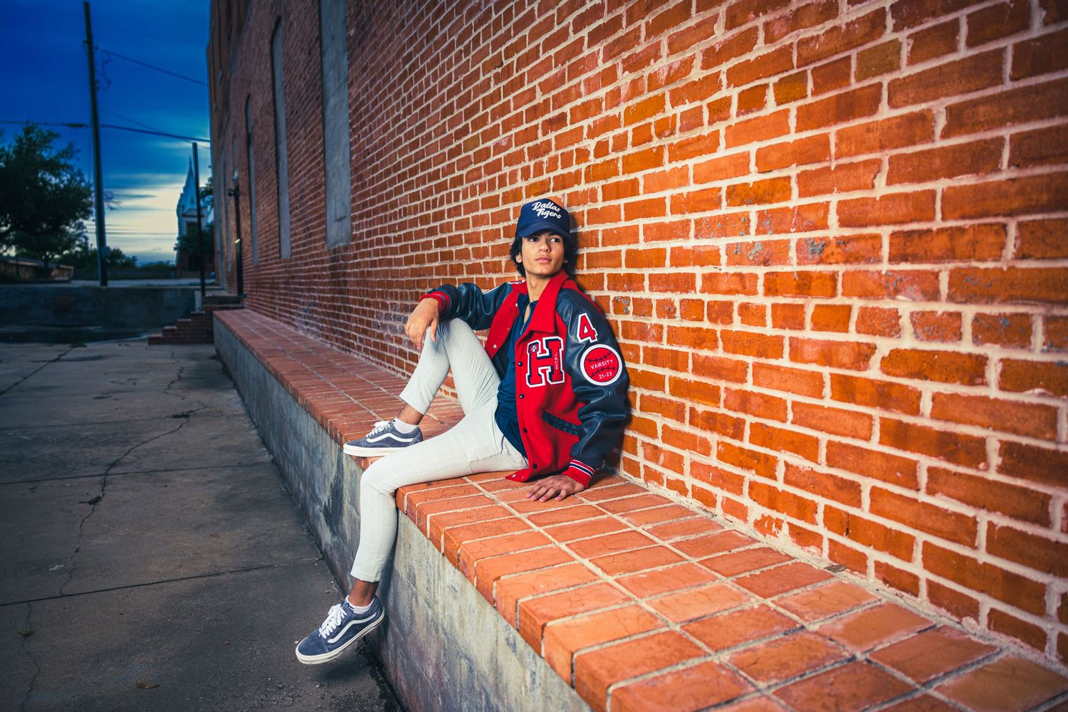 Baseball player in Cubs jersey sitting on brick ledge at sunset.