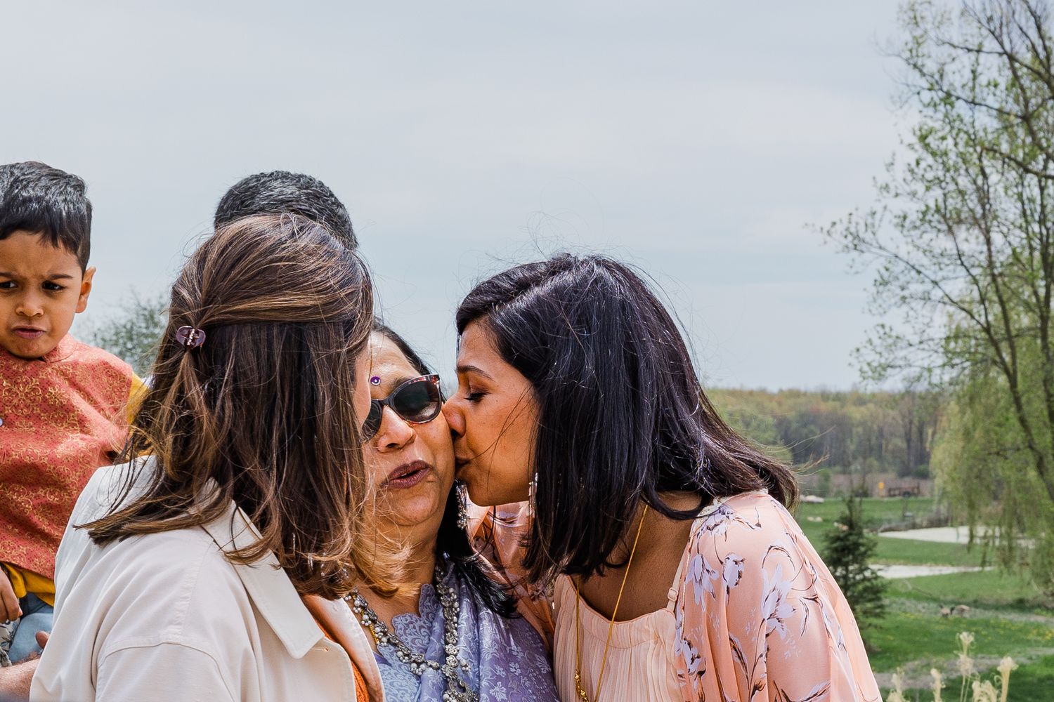 Three people in casual attire share an intimate moment outdoors with trees in the background.