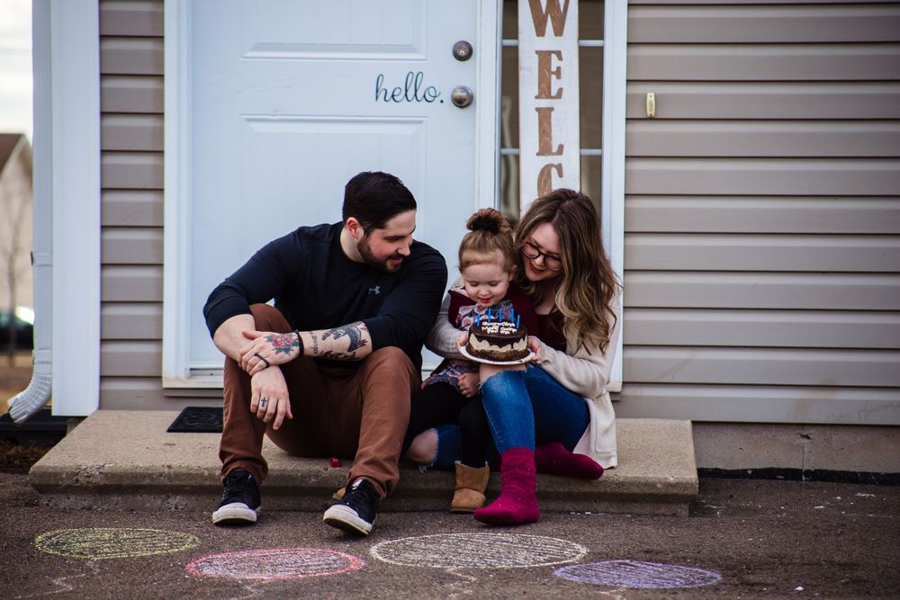Family members sitting on front porch steps with welcome sign visible.