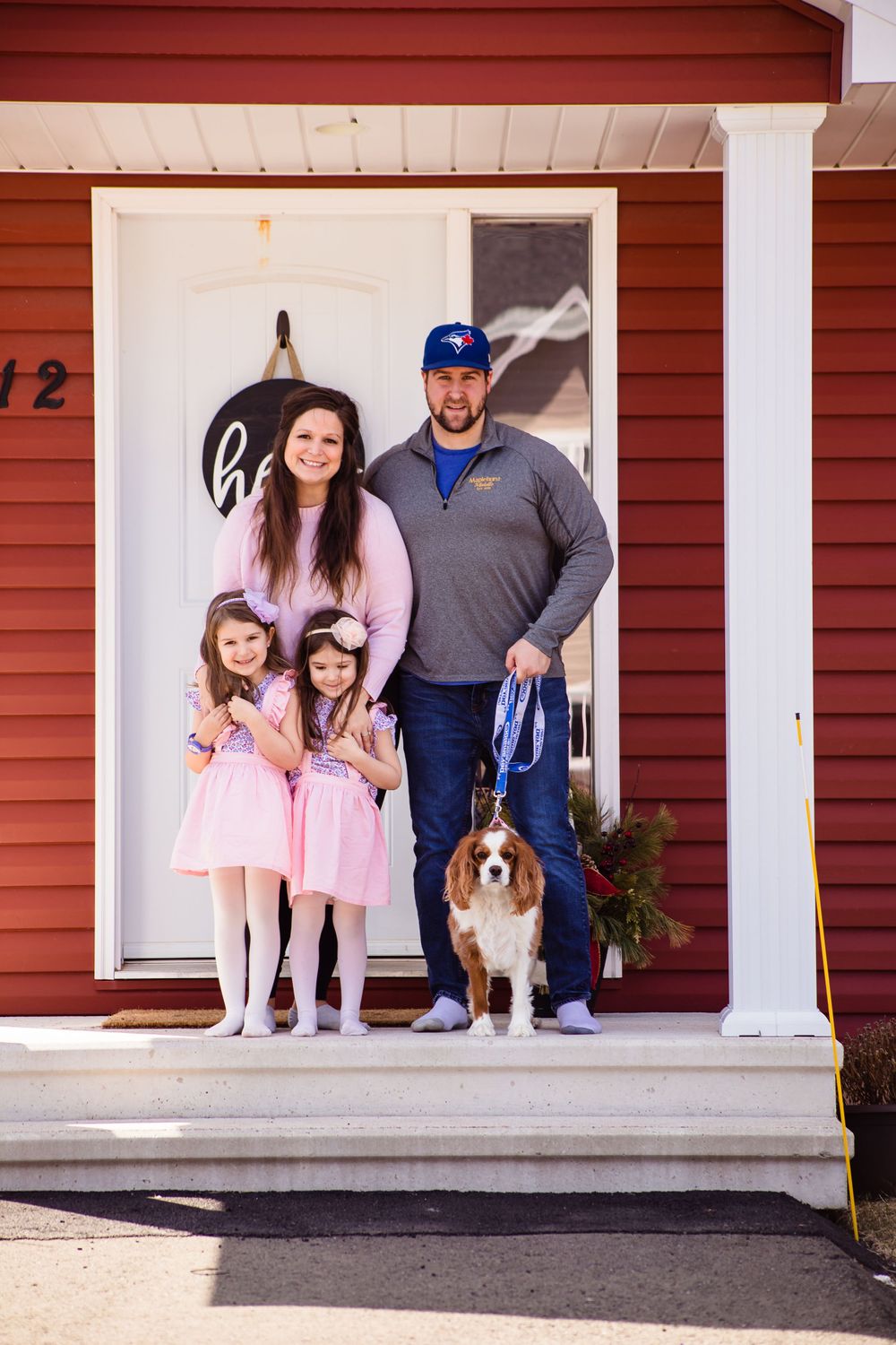 Family with dog standing on red house porch wearing pink dresses.