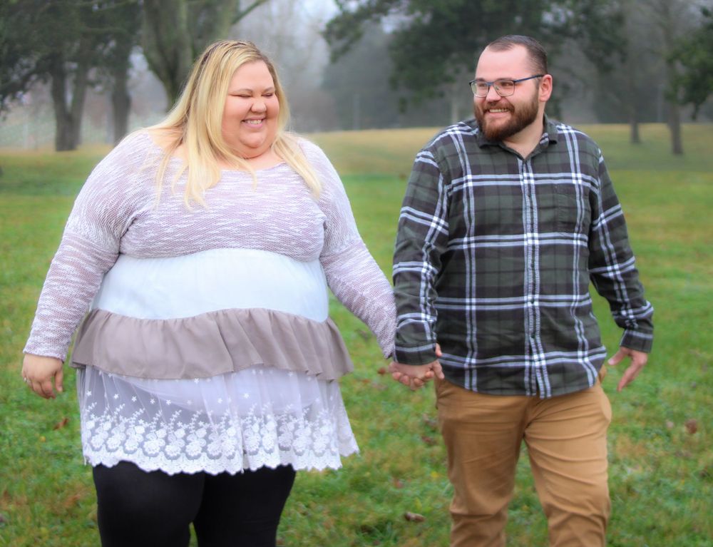 Couple walking and laughing together in casual attire on grassy field.