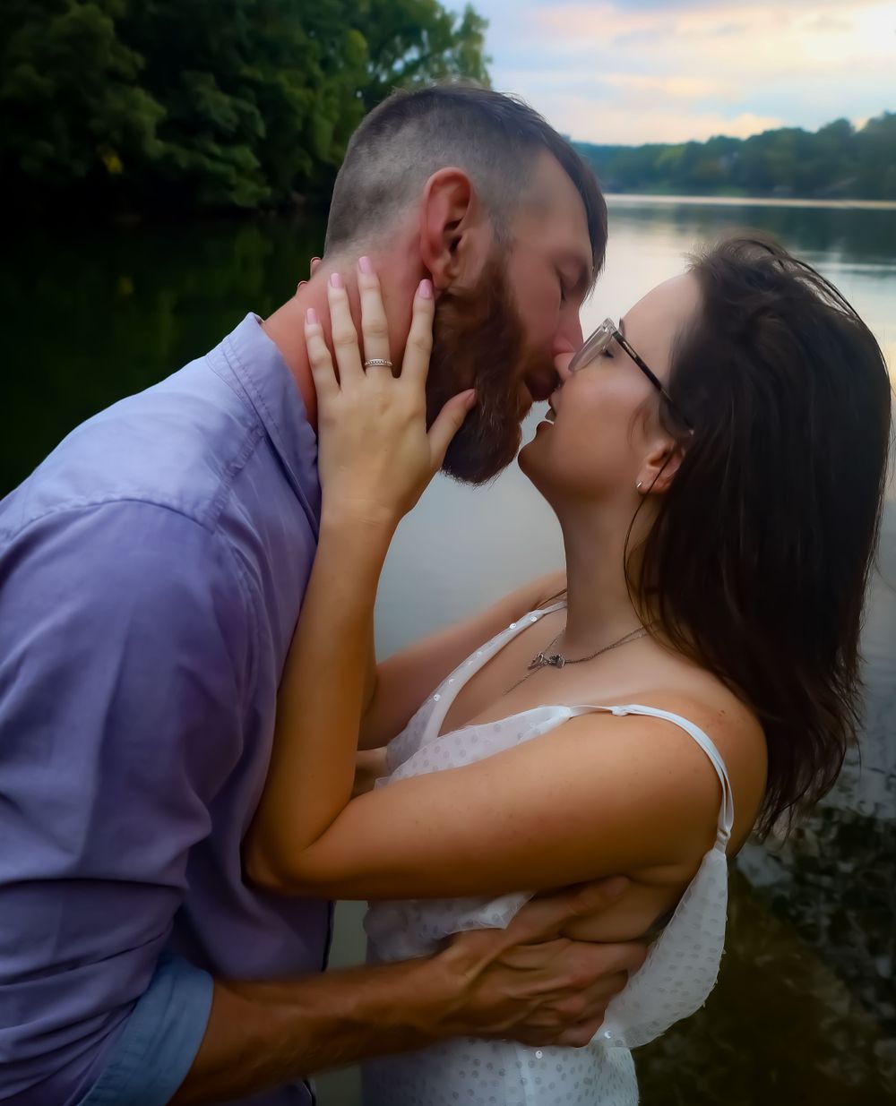 Intimate romantic moment captured between couple by lakeside during sunset.