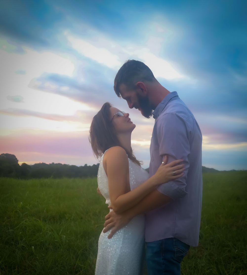 Couple sharing tender moments at sunset in an open field with dramatic sky.