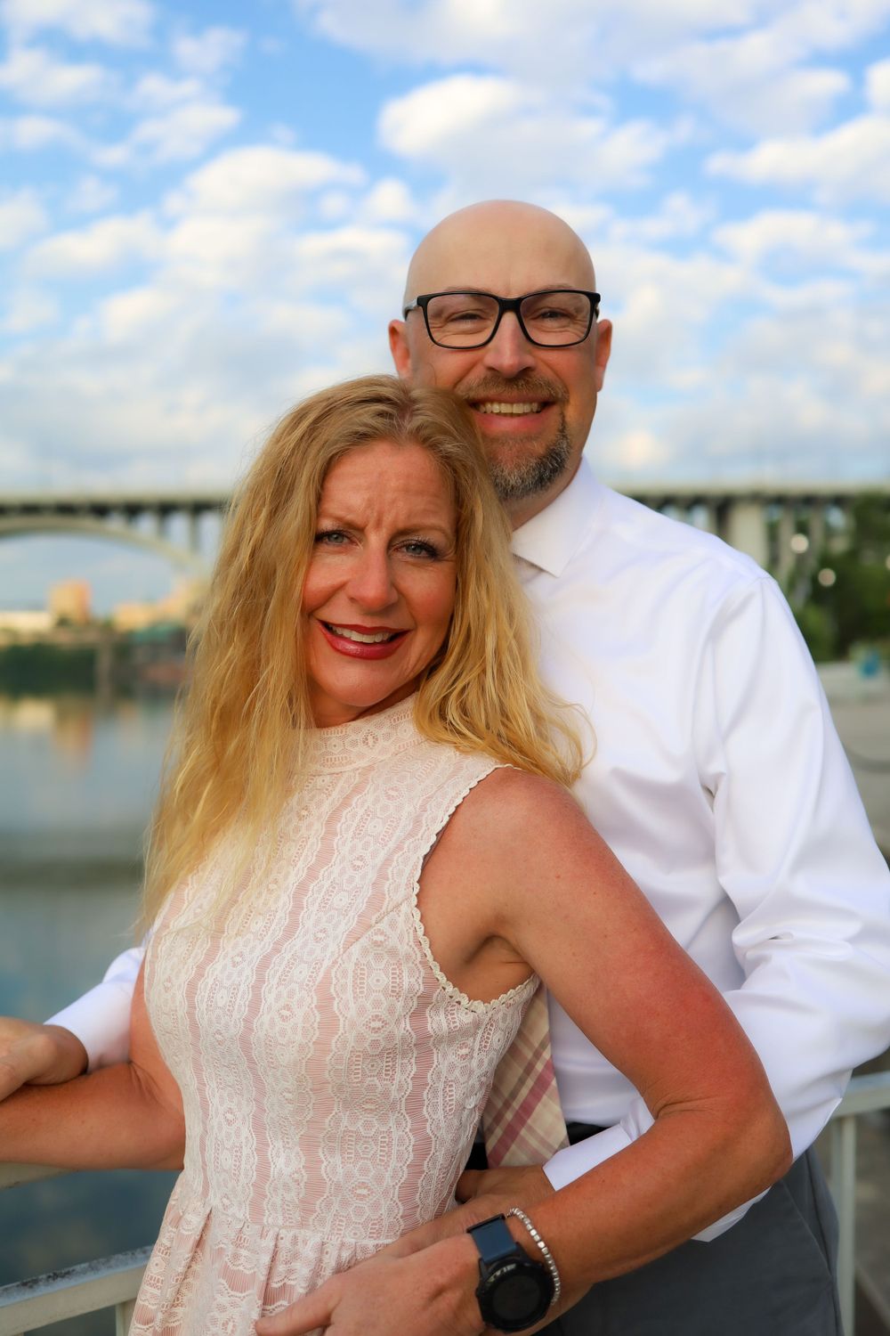Romantic couple portrait on waterfront with bridge and blue sky in background.