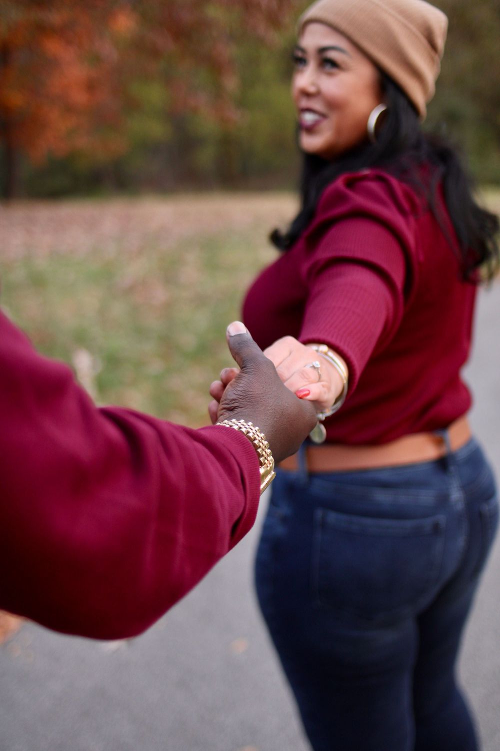 Person in burgundy sweater and tan beanie dancing joyfully outdoors in autumn.