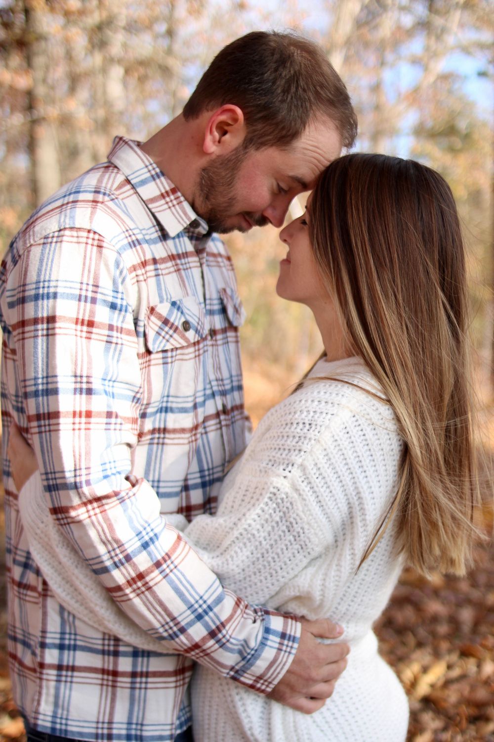Romantic couple embracing in autumn woods wearing plaid and white sweater.
