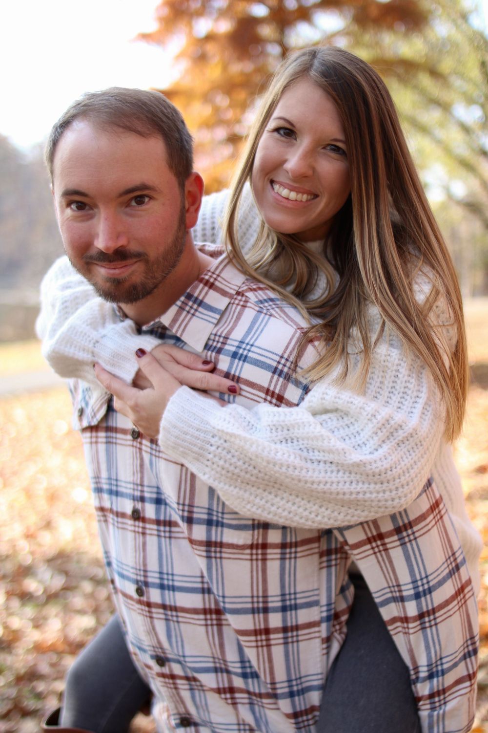 Playful couple embracing and laughing in autumn setting wearing plaid and white knit.