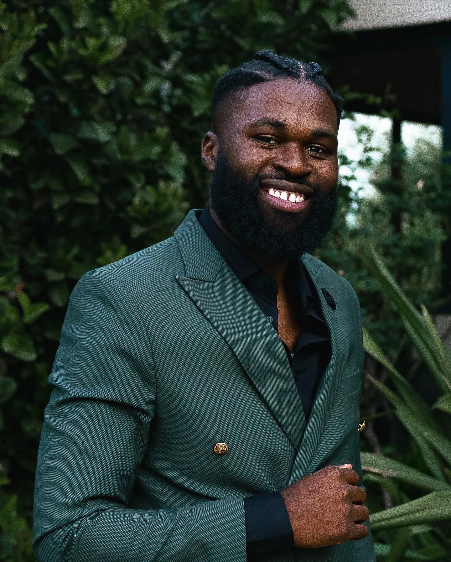 Portrait in dark green blazer with beard against garden background.