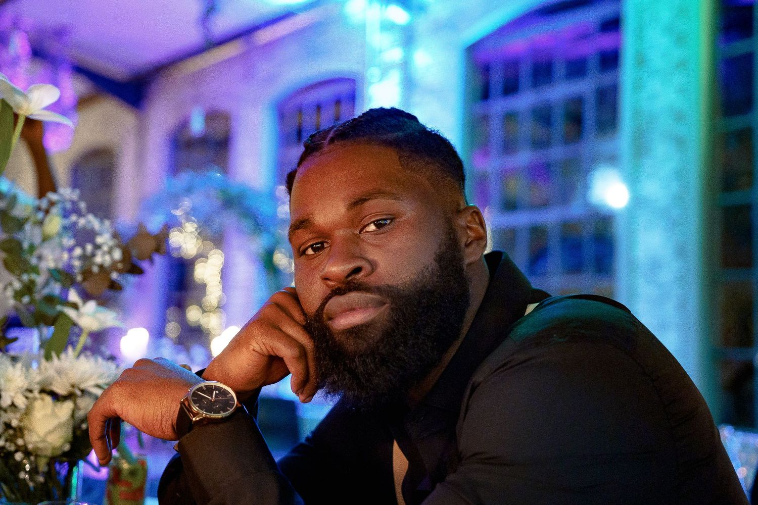 Person in dark attire poses thoughtfully in a dimly lit venue with blue ambient lighting.