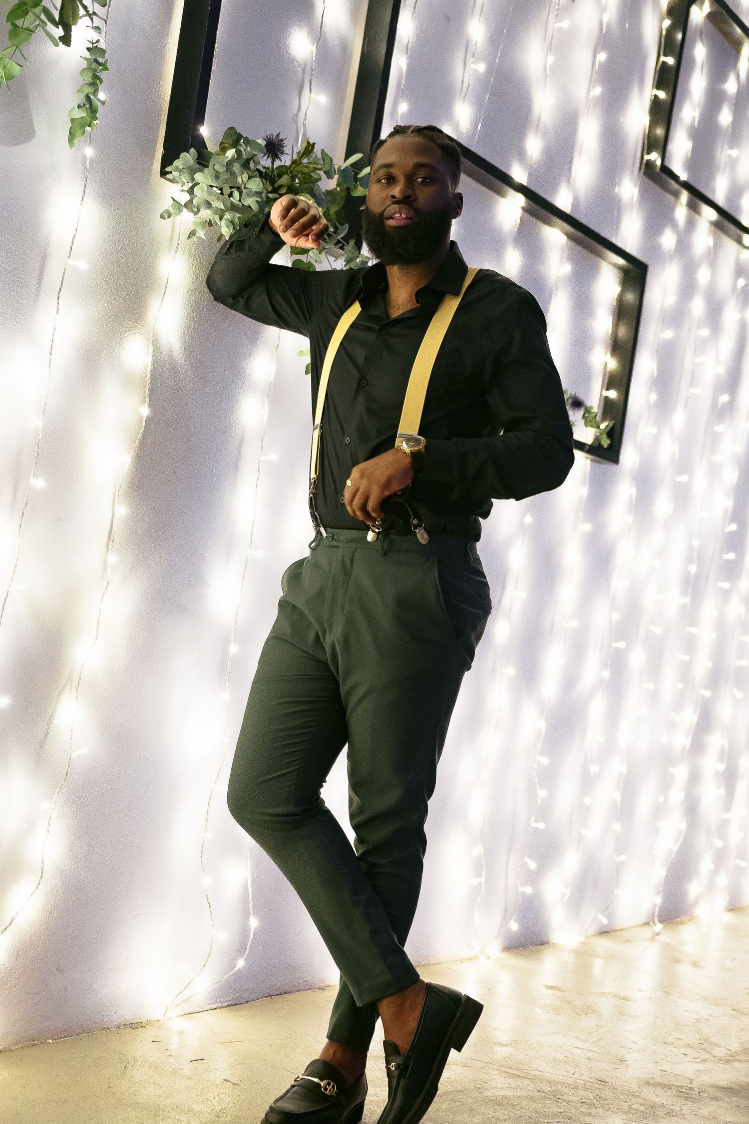 Stylishly dressed person poses against a white backdrop with twinkling lights and floral decorations.