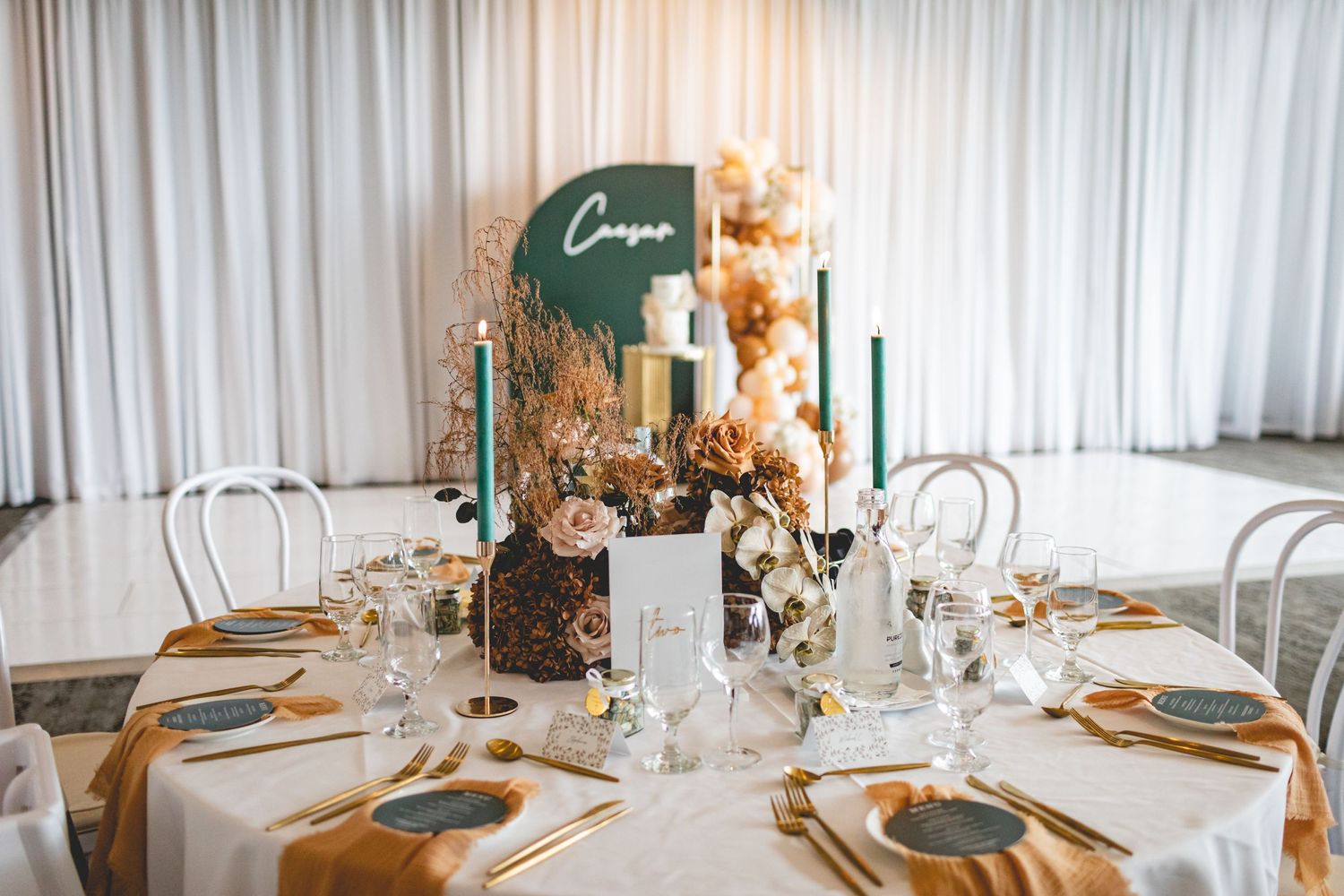 Round dining table with elegant place settings, green accents, and warm autumn-toned floral centerpiece.