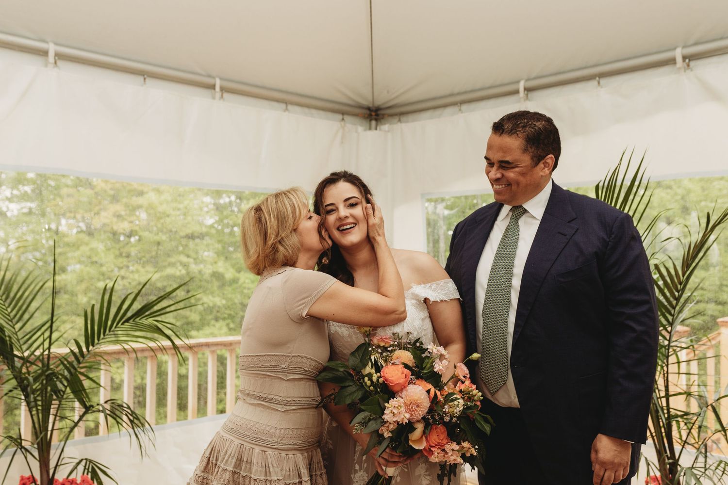 A celebratory moment under a white tent with peach flowers and greenery.