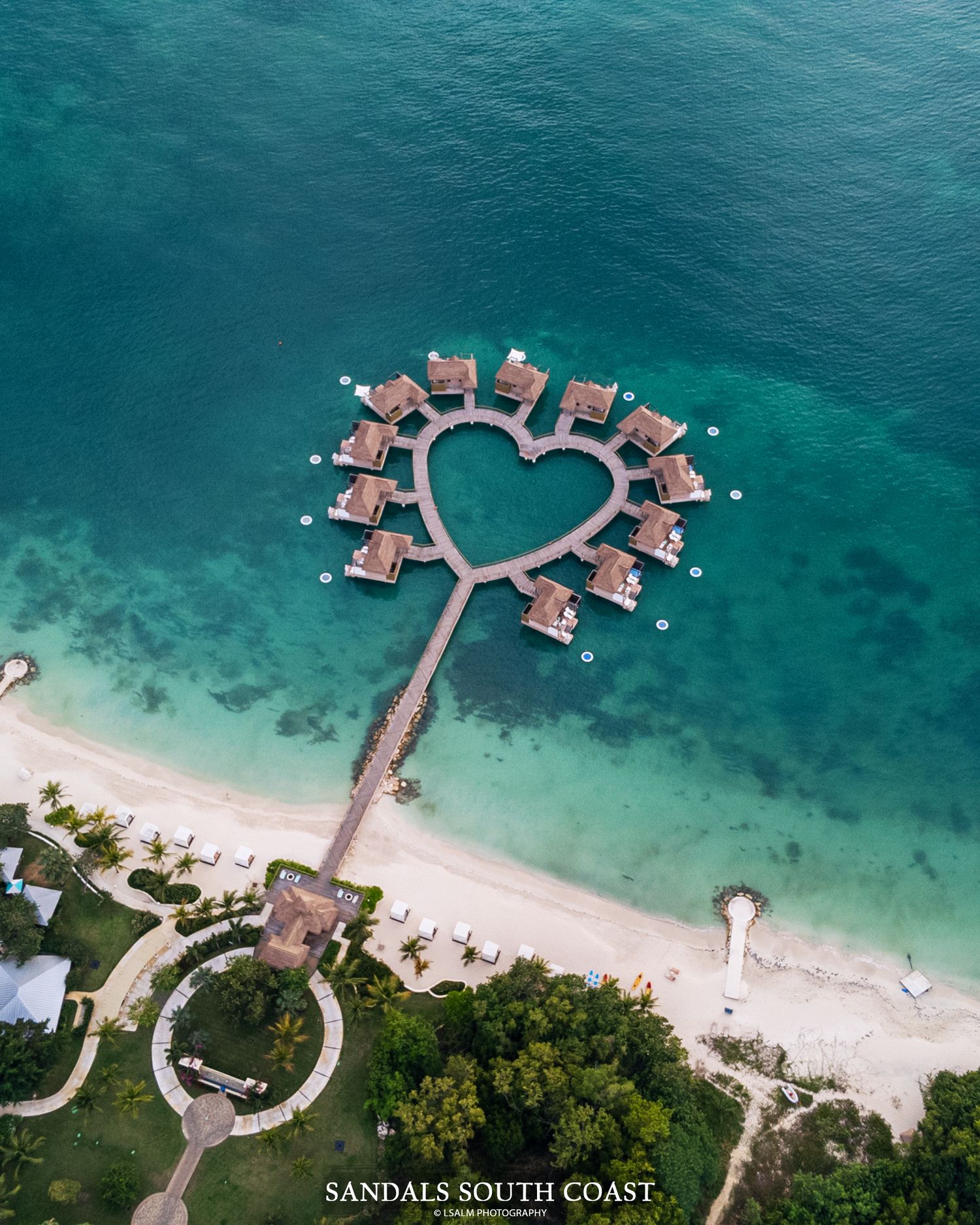 Aerial view of heart-shaped overwater bungalows in turquoise ocean.