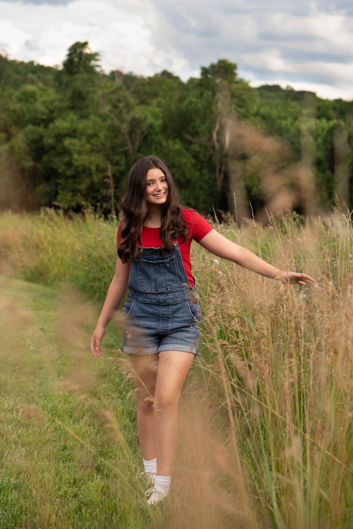 teen girl smiles as she walks, brushing wild grass with her hand