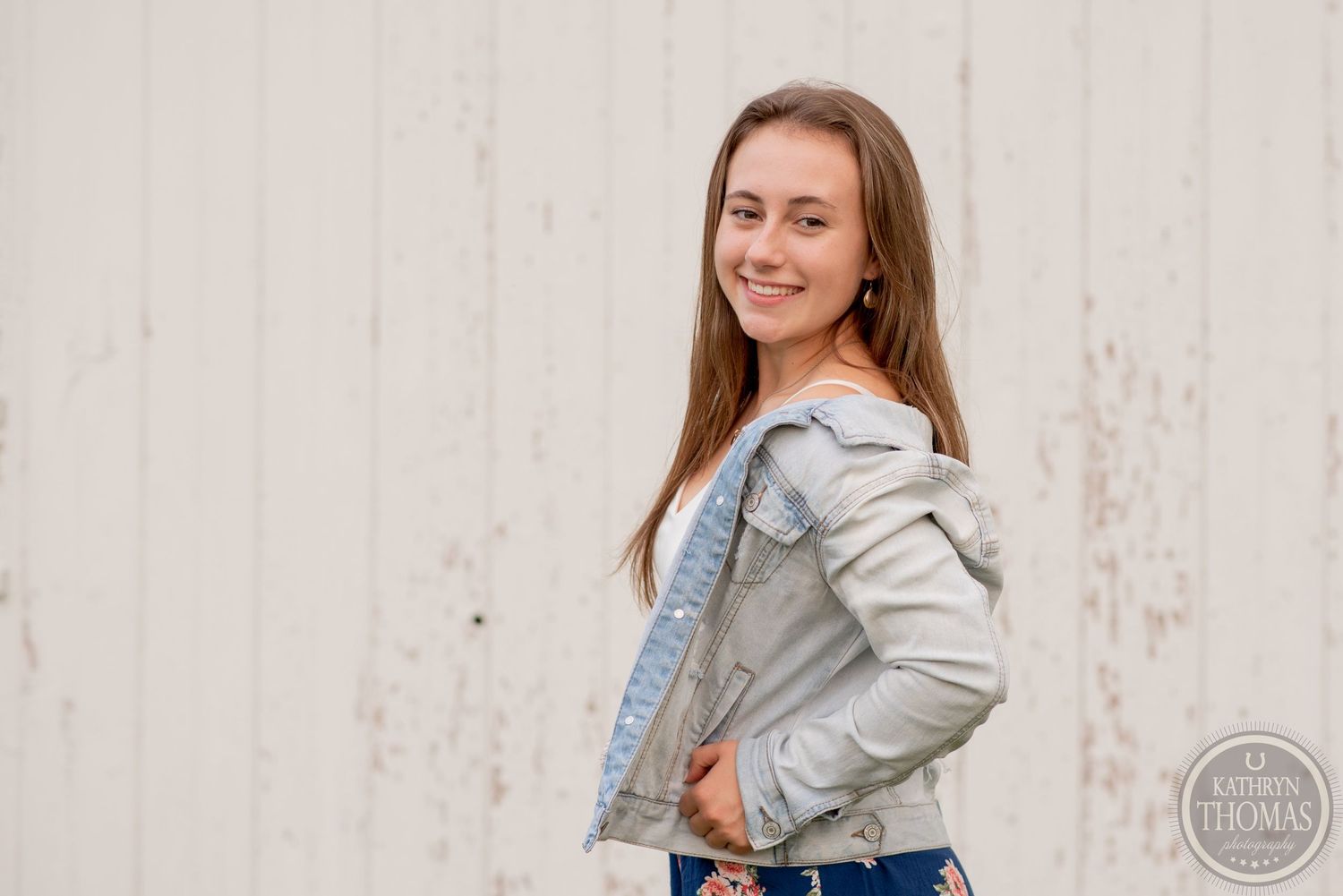 Someone in denim jacket poses against white wall during outdoor photoshoot.