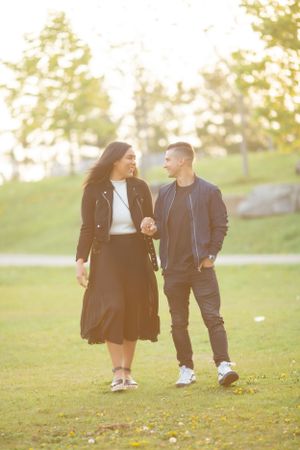 Newly engaged couple walking together in park during sunset.
