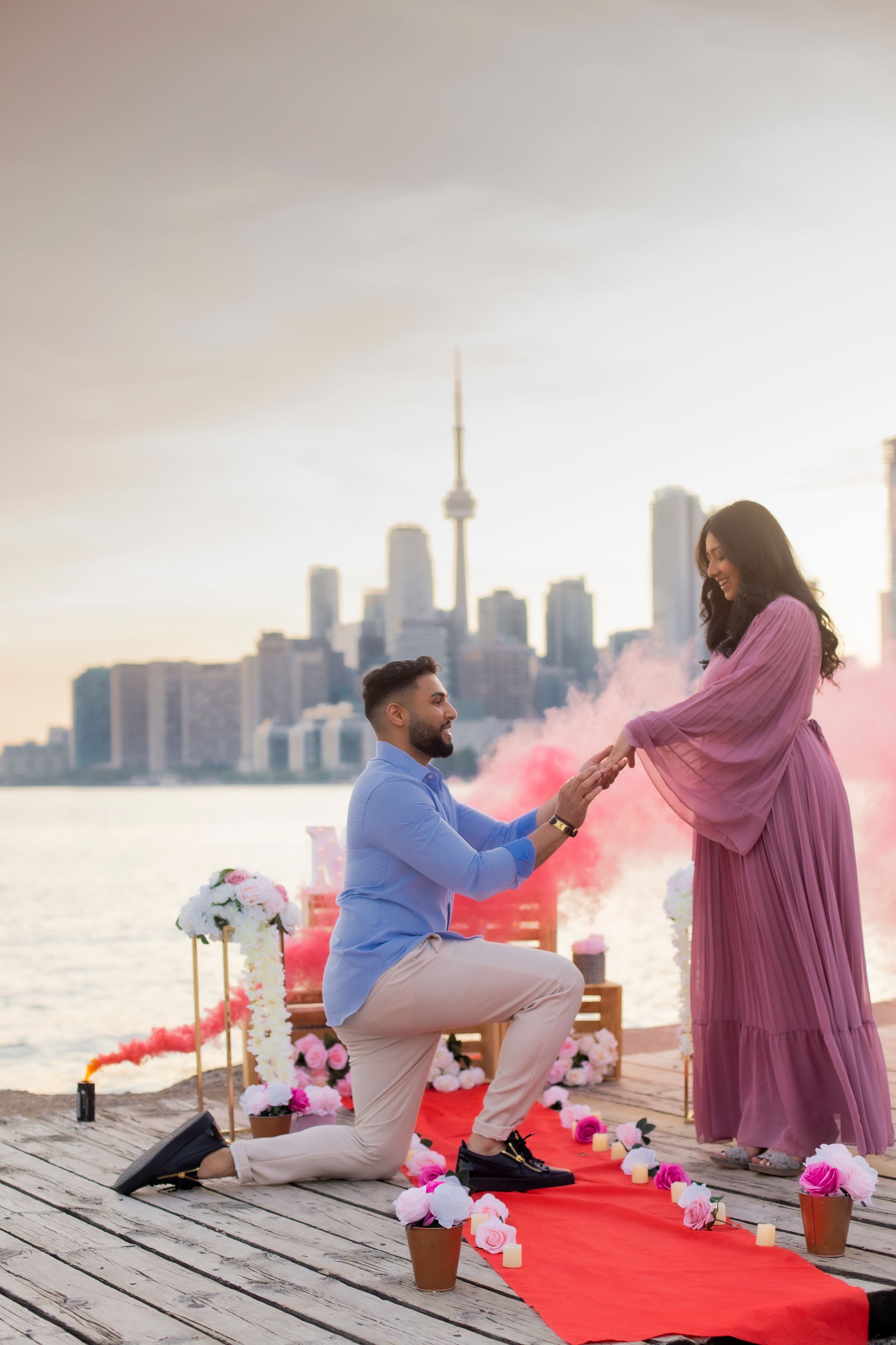 Proposal scene with smoke effects and red carpet on Toronto pier during golden hour.