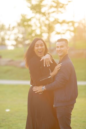 Happy couple showing off engagement ring in park during golden hour.