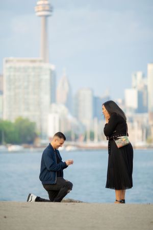 Marriage proposal moment at waterfront with Toronto's CN Tower in background.
