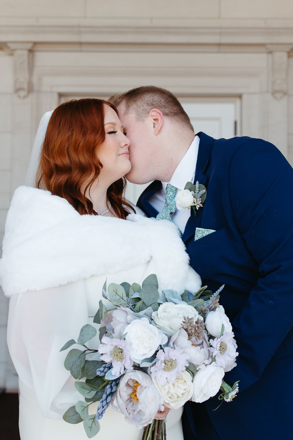 Newlyweds share intimate moment while bride holds elegant white and purple bouquet.