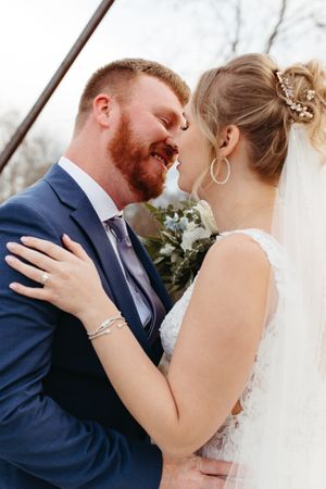 A wedding couple shares an intimate moment on a bridge with the bride wearing delicate jewelry.