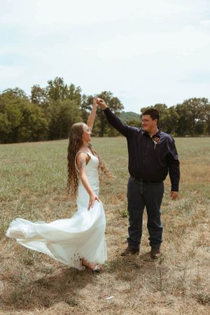 A couple dances in a rustic field as the bride's dress flows in the breeze.