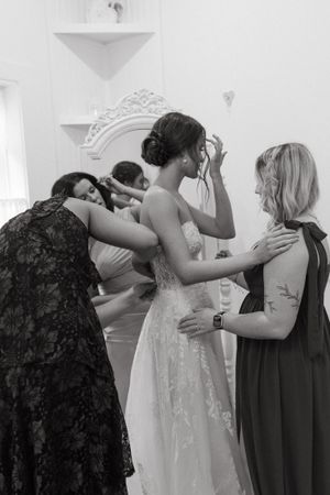 Emotional black and white image of bride getting ready with help from bridesmaids.