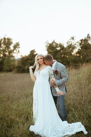 Intimate wedding portrait of couple embracing in golden field at sunset with elegant white lace gown.