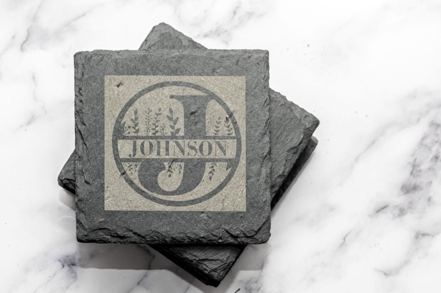 Gray slate coasters with vintage monogram design on marble surface.