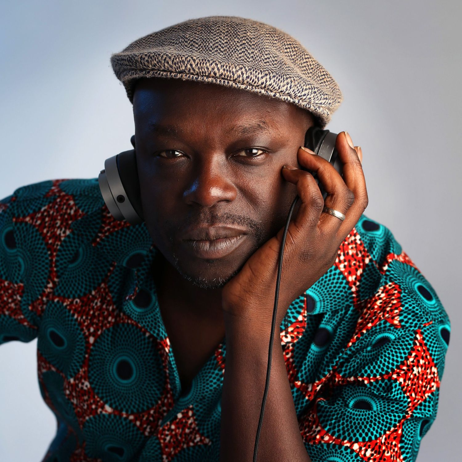 Portrait of someone wearing headphones, tweed cap and colorful patterned shirt against light background, in Stoke Newington studio.
