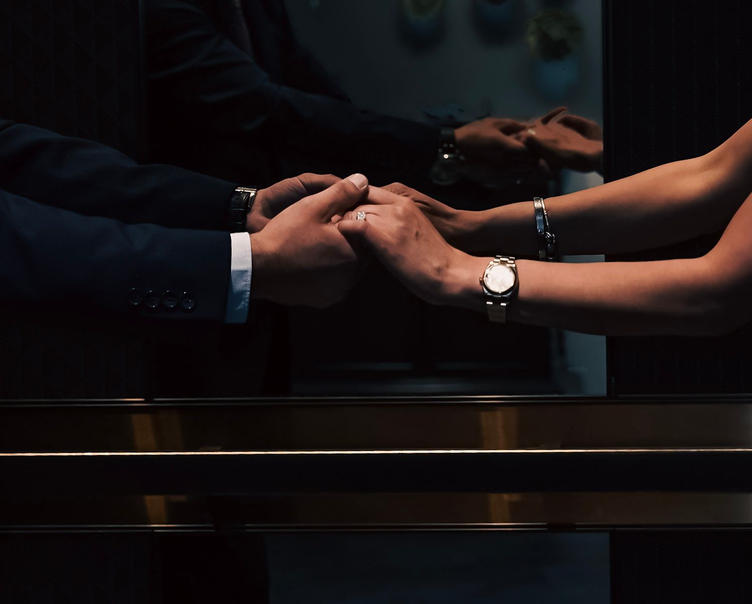 Close-up of hands touching across a dark table with watches visible in dramatic lighting.