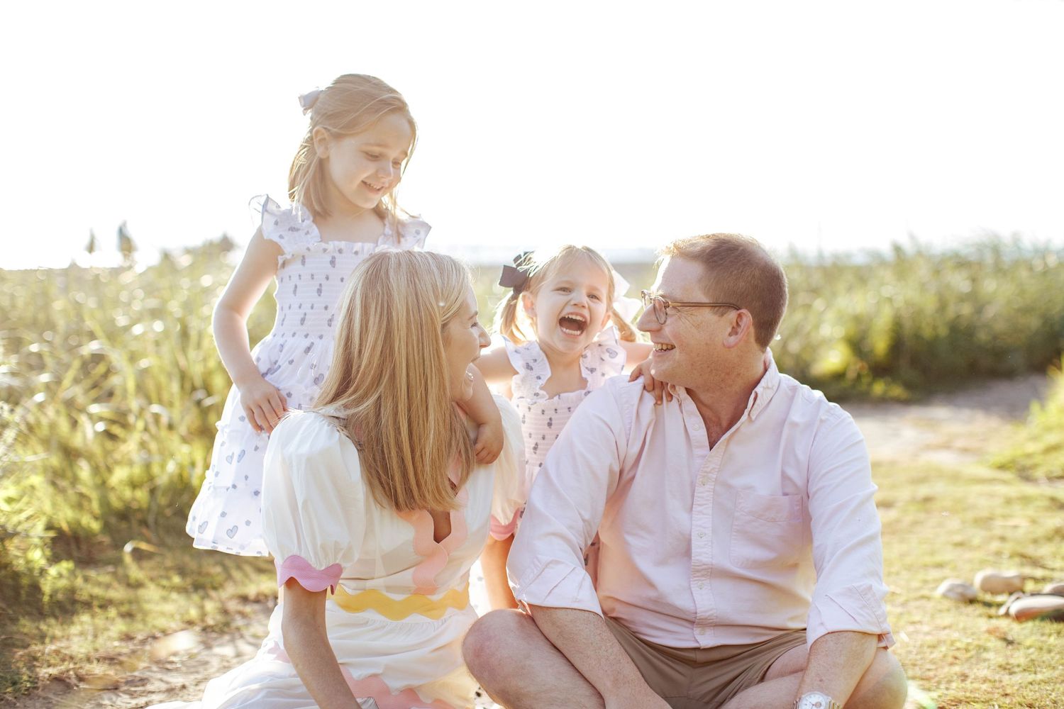 everett family photography: a mom and dad sitting at carkeek park, their two daughters are laughing behind them