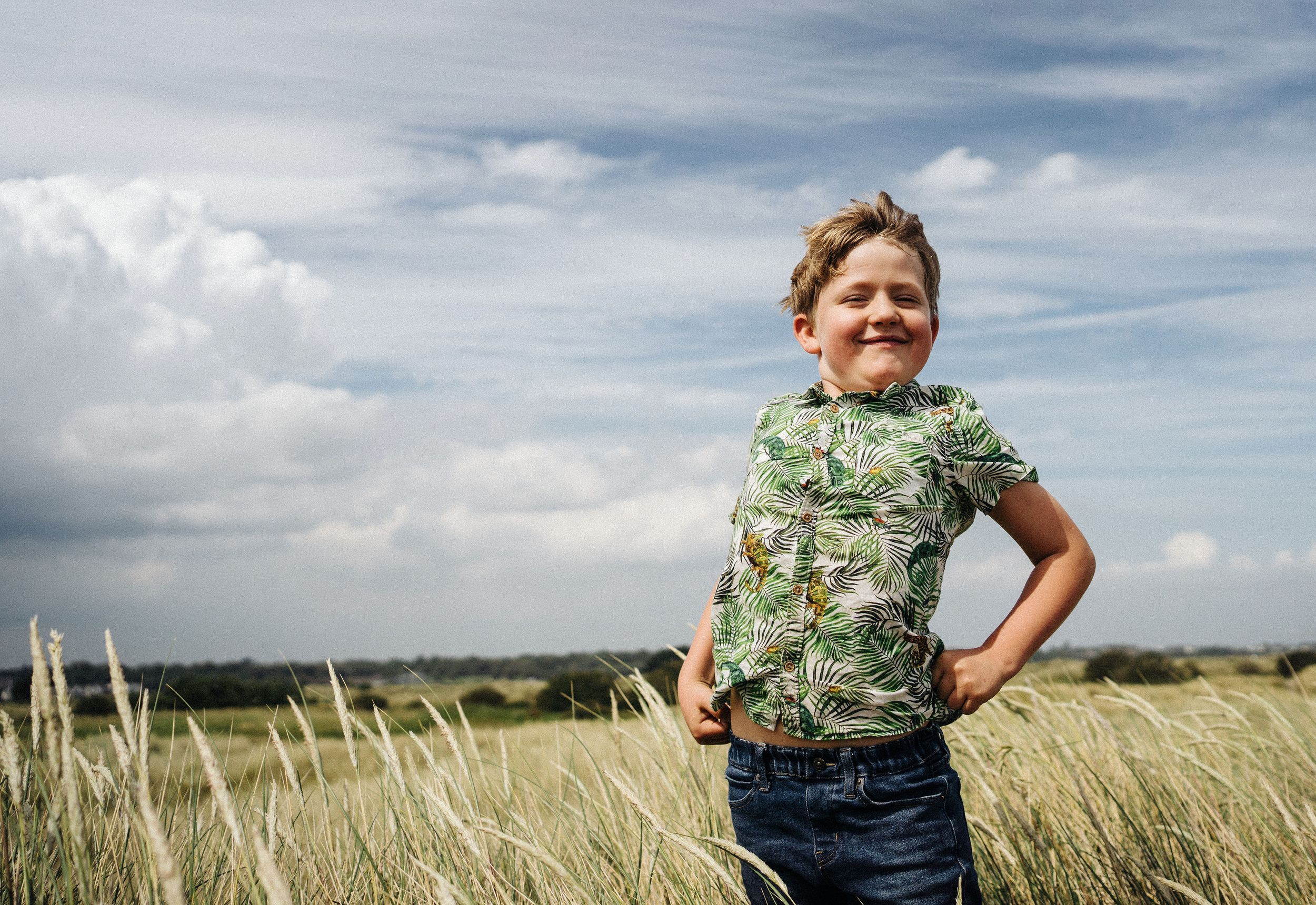A child stands confidently in a flowered shirt against a dramatic sky and grassland backdrop.