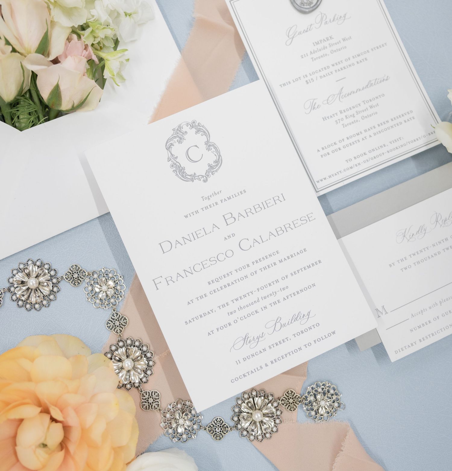 Elegant white wedding invitation suite with floral details and crystal jewelry accents on a light blue background.