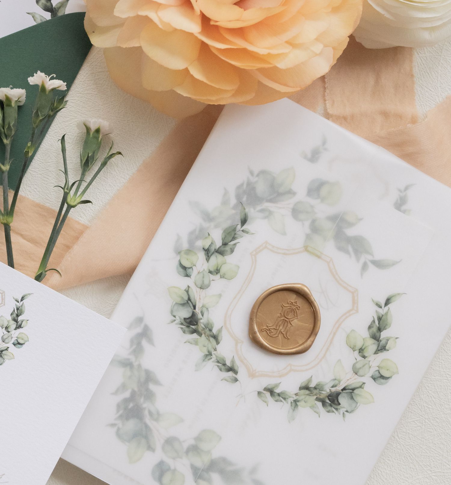Wedding invitation with delicate green wreath design and gold wax seal.