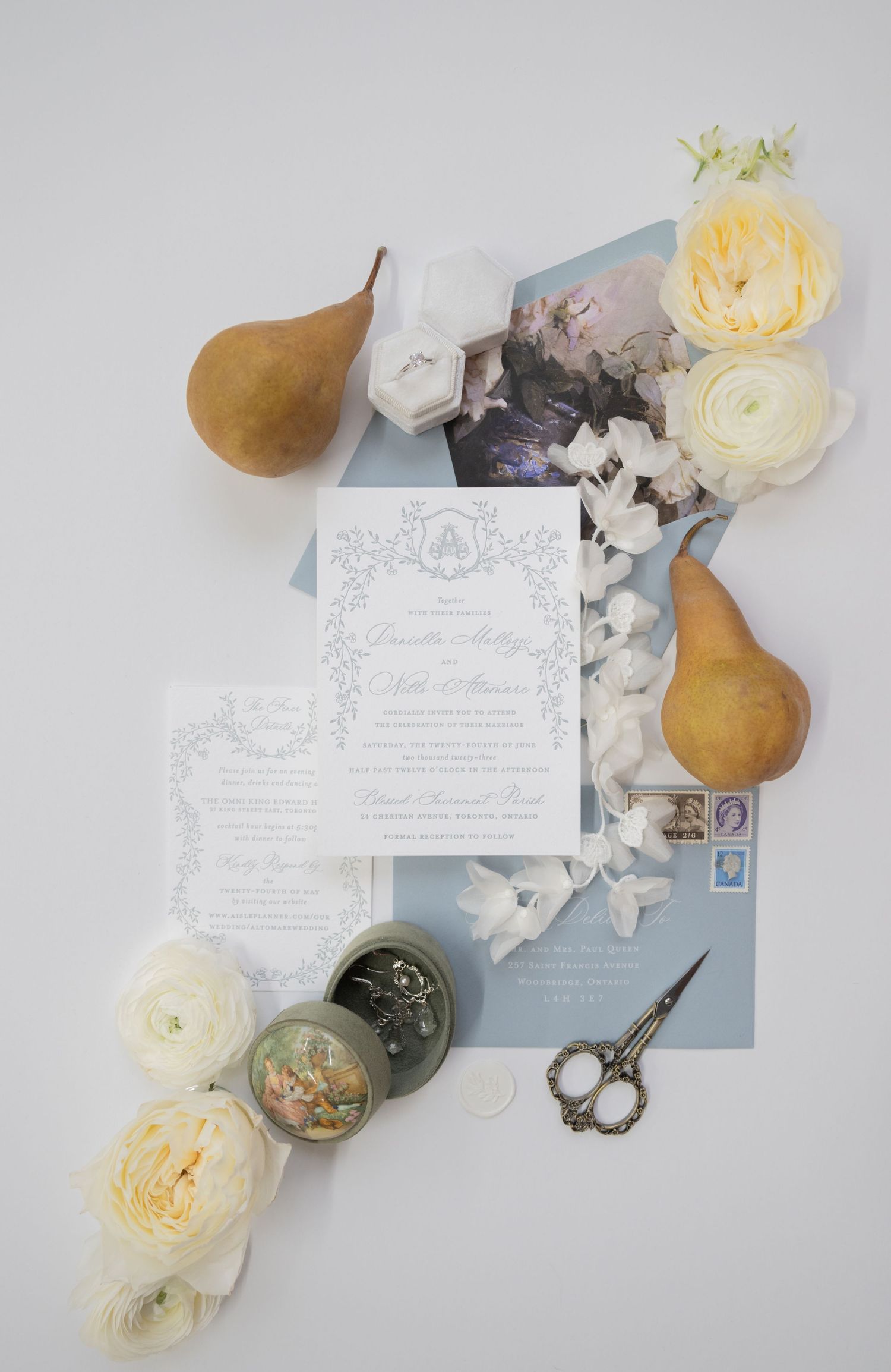 Wedding stationery flatlay with pears, roses, and vintage scissors on light background.
