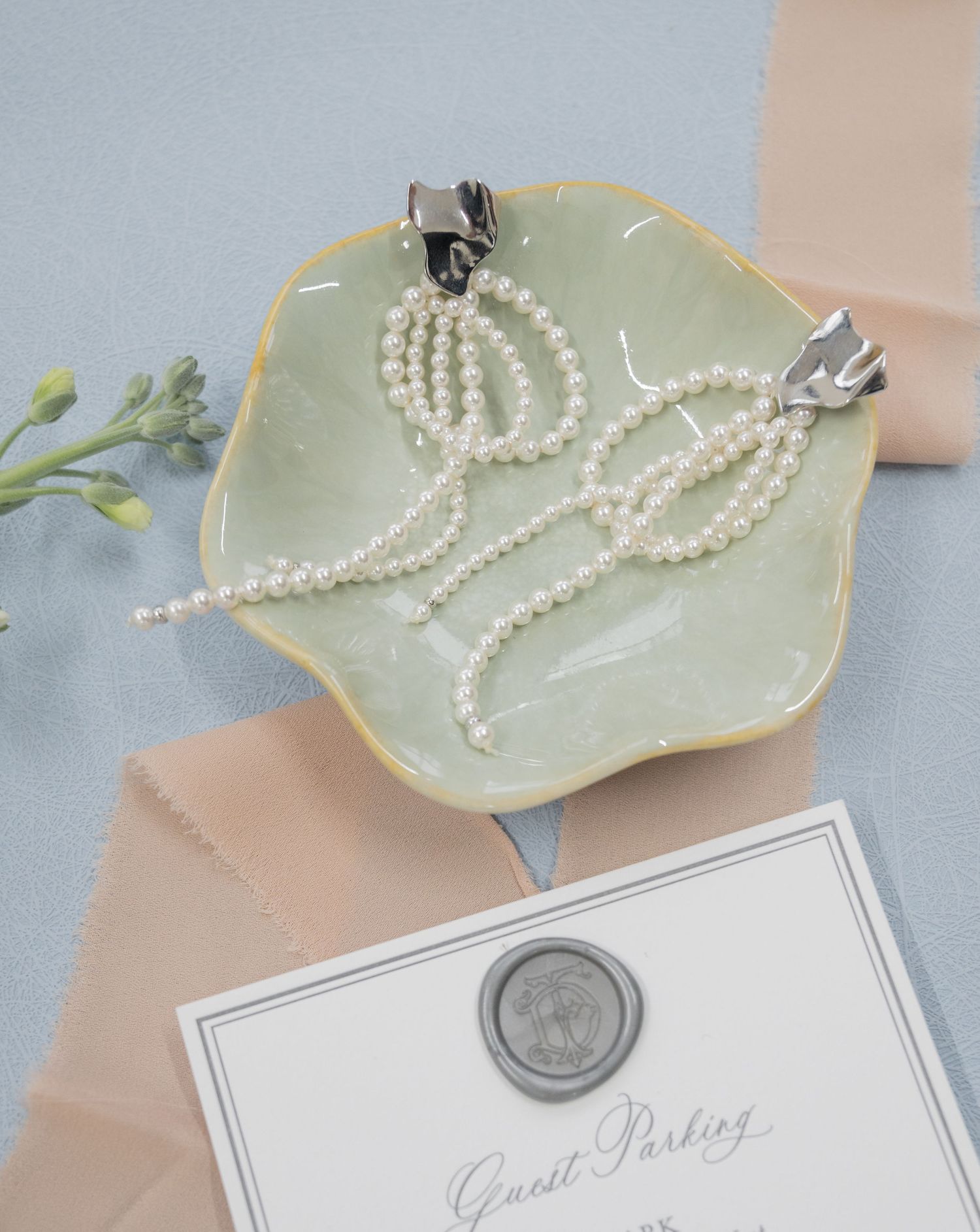 Pearl necklace displayed on mint ceramic dish with wedding invitation and wax seal below.
