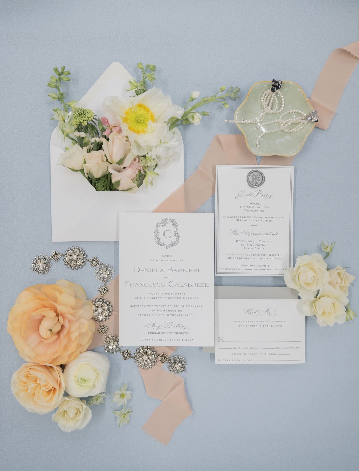 Wedding stationery suite with peach roses and crystal accessories arranged on a pale blue surface.