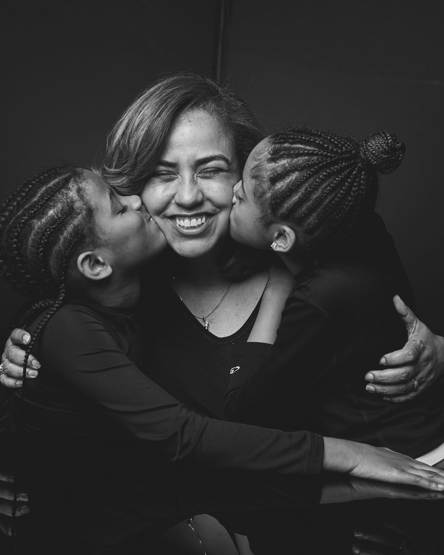 Black and white photo of two children kissing a smiling woman on both cheeks in a warm embrace.