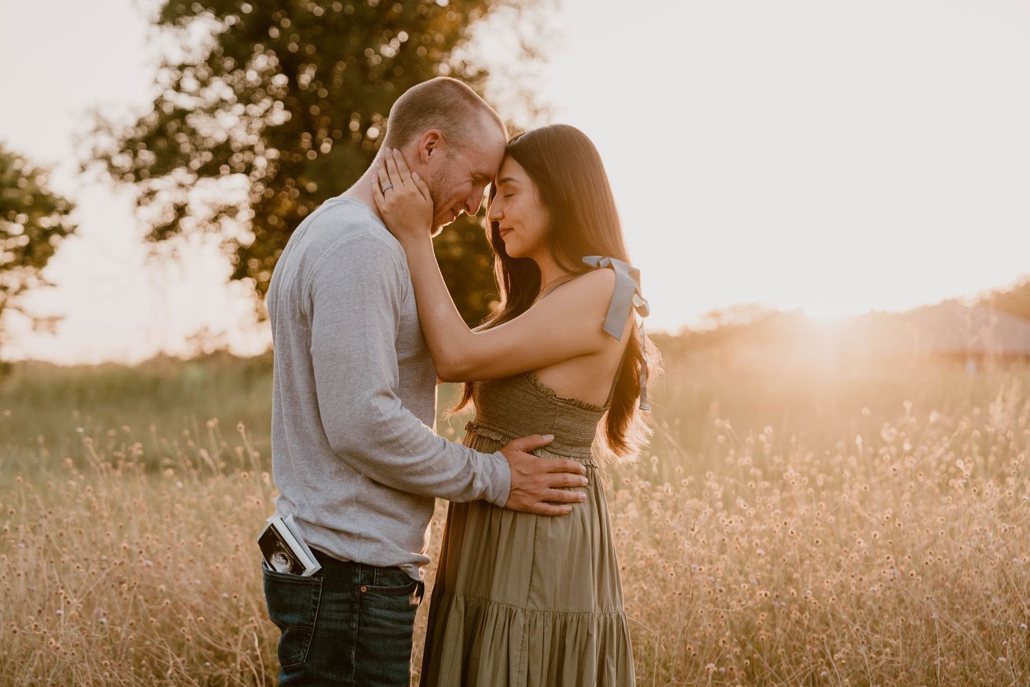 Couple embracing each other in a field. Baby announcement session in a field in Prosper Texas. Ultrasound in mans pocket